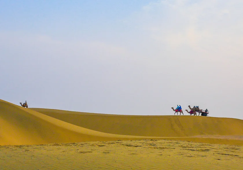 Camel riders crossing the dunes on a desert safari near Jaisalmer